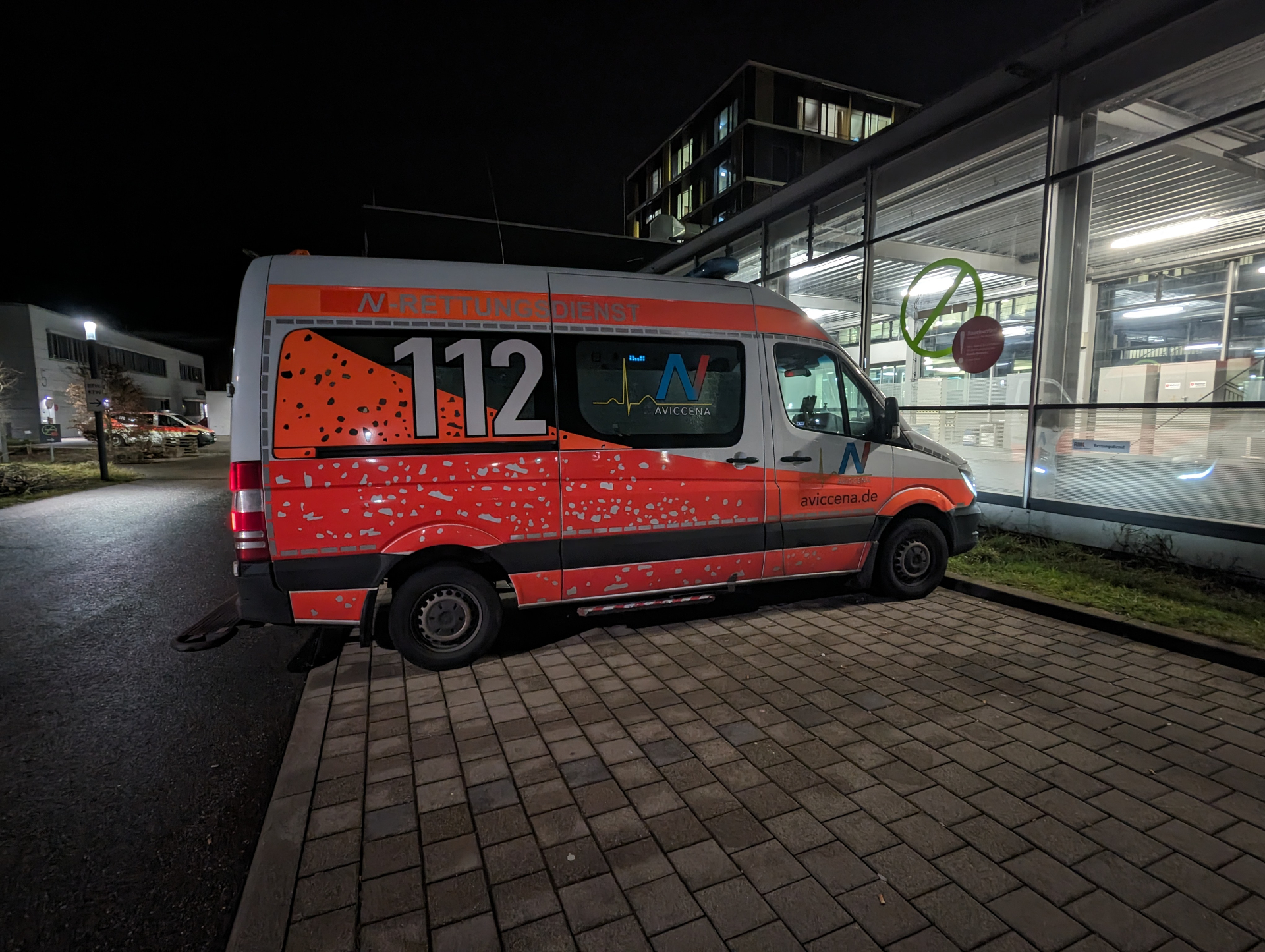 Aviccena Krankentransport vor beleuchtetem Klinikgebäude bei Nacht